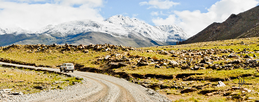 A dirt road with snow capped mountains in the background.